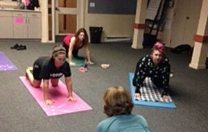 3 teen girls in a Yoga Outreach-led class practise breathing in time with movement.