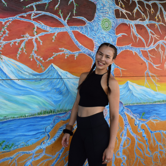 Boxing coach and Yoga teacher, Ivy Richardson, founder of Red Girl Rising, stands powerfully in front of colourful mural wearing work out clothes